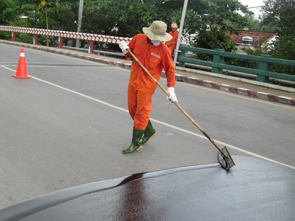 Manual rubber squeegee application of TL-2000 on road pavement in Vietnam